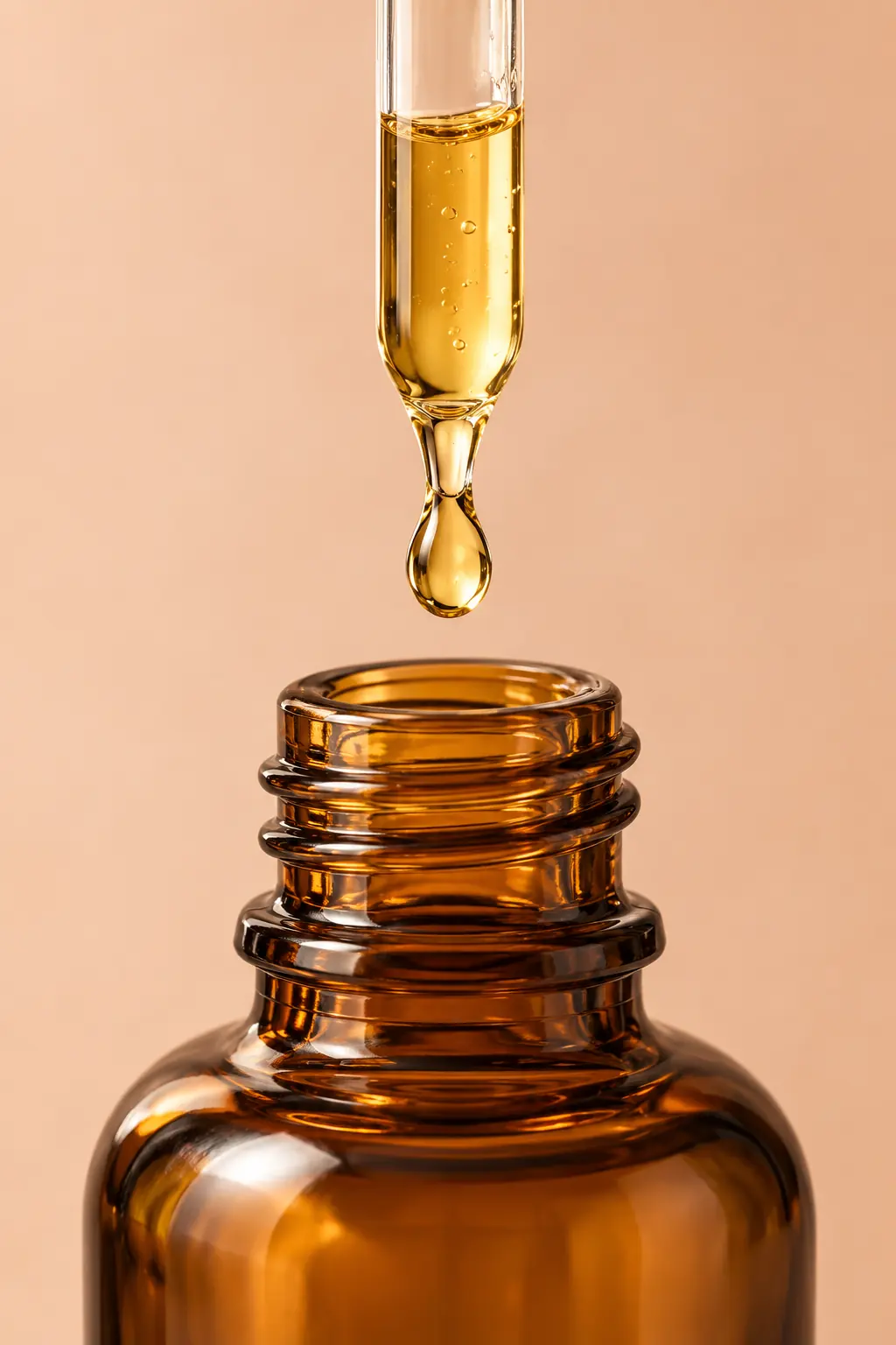 Glass pipette releasing a golden drop into an amber bottle